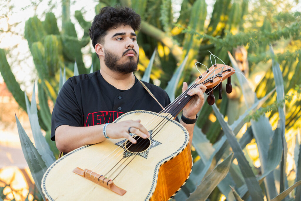 Young bearded man plays guitarró in front of agaves