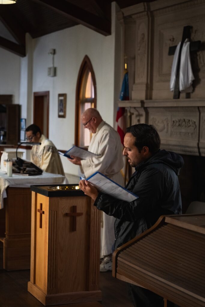 man with hymn book singing with deacon and priest in background