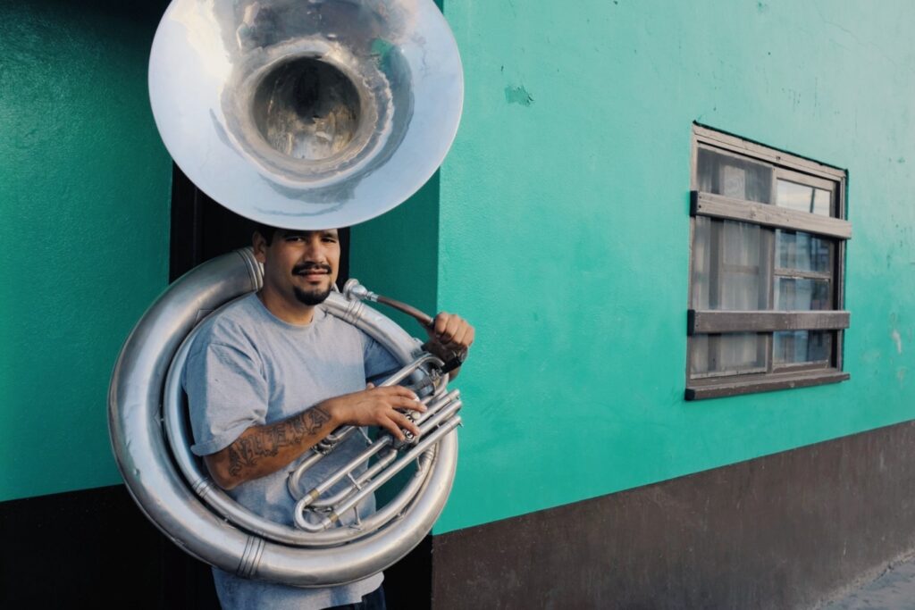 Man with sousaphone stands against a teal wall