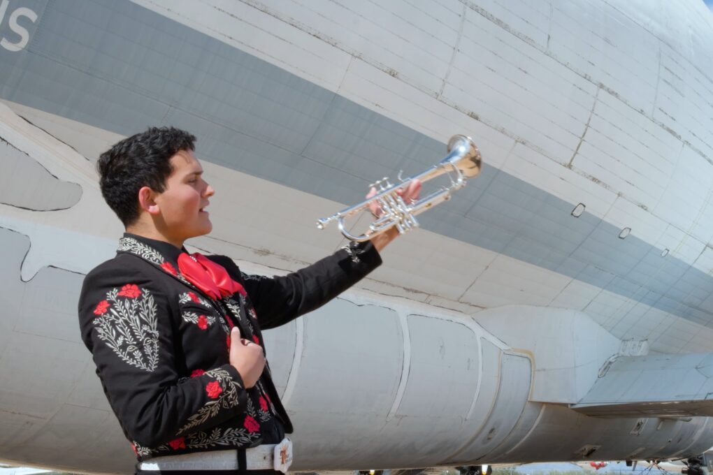 Young trumpet player in mariachi suite in front of an airplane