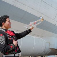 Young trumpet player in mariachi suite in front of an airplane