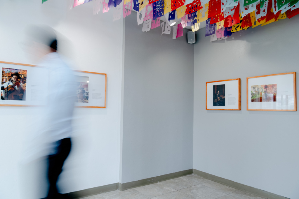 Blurred gallery visitor among framed photographs and papel picado